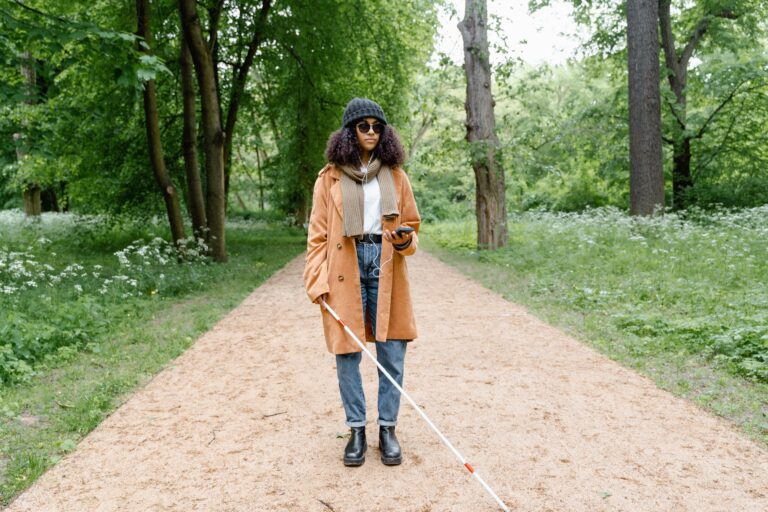 Femme &eacute;l&eacute;gante en manteau explore un parc verdoyant avec une canne, utilisant son smartphone pour se guider
